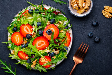 Vegan strawberry and herbs salad with arugula, blueberries and walnuts on black background. Top view