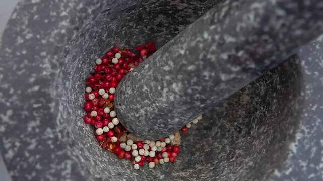 Super close-up of spicy white and rose peppercorns falling into the grey stone mortar in slow motion. High quality 4k footage