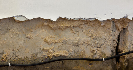 Weathered concrete wall with exposed wire, cracked plaster, and signs of moisture damage, revealing structural issues.