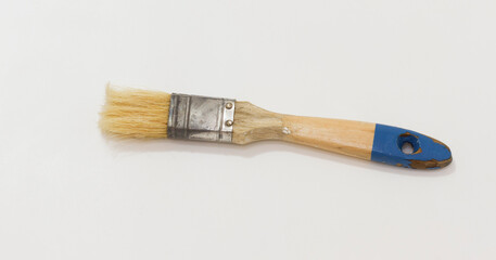 A worn paintbrush with wooden handle and blue paint, lying flat on plain white background.