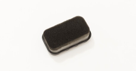 Short Rectangular foam sponge with black surface, commonly used for shoe polish or cleaning. © Issah