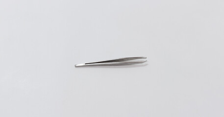 A silver metallic tweezer lying flat on plain, light background, suitable for medical or grooming contexts.
