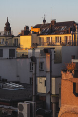 Golden hour on Prague rooftops, capturing the warm glow of the sun on residential buildings with satellite dishes and a historic dome in the background.