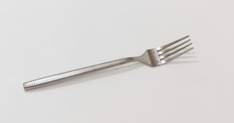 A simple stainless steel fork with four tines, resting on light colored surface, minimalistic design.