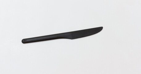 A simple black plastic knife on plain white background, perfect for minimalist or kitchen related content.