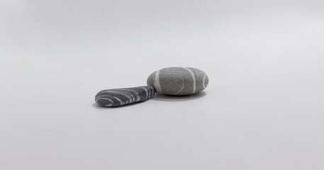 Minimalistic composition of two smooth, striped pebbles placed on clean, neutral background.