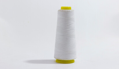 A close up of white sewing thread spool with yellow ends, isolated on light background.