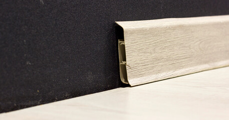 Close up of plastic skirting board with cable management feature, attached to dark wall and light floor.