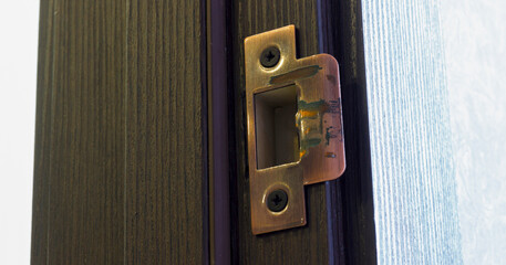 Close up of door strike plate on wooden frame with visible wear and scratches.