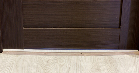 A close up of brown wooden door with floor threshold on light wooden flooring.