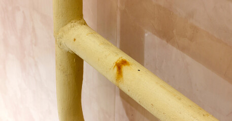 Yellow painted pipes with rust stain against light colored textured wall, highlighting industrial decay.