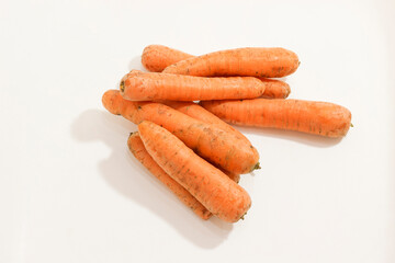 A pile of fresh, unwashed carrots with rustic appearance on white background, showcasing their natural texture.