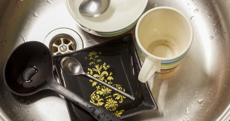 Dirty dishes in kitchen sink, including mug, bowls, spoons, and black plate with yellow patterns.
