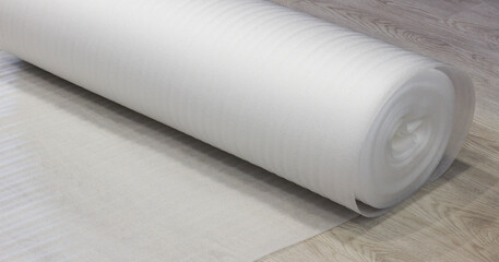 Rolled white foam underlay on wooden flooring, perfect for insulation, soundproofing, and cushioning.