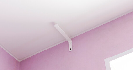 White bracket mount attached to ceiling corner, featuring lavender walls in minimalist room setting.