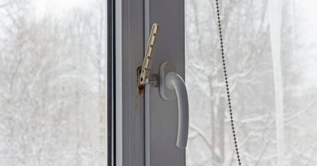 A white plastic window handle with slightly rusted lock mechanism, viewed from inside during winter.