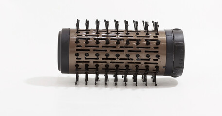 Close up of cylindrical hair styling brush attachment with retractable bristles on white background.