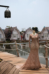 A long-sleeved bridal kebaya in light brown, adorned with elegant embellishments, perfect for a traditional Indonesian wedding from West Java’s Sundanese culture. The background features a serene lake