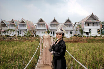 The bride's preparation is complete, with her makeup ready for a traditional Sundanese wedding from West Java. In the background, the kebaya she will wear and the picturesque view of rice fields and a