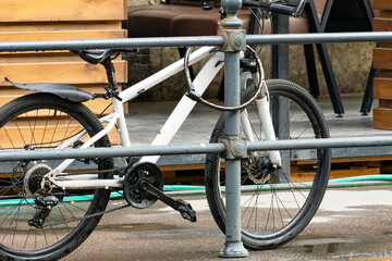 parked white bicycle on the street secured against theft with a steel cable and lock