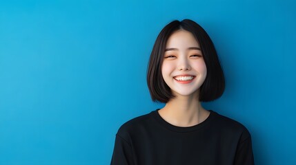 Fototapeta premium A smiling person with short hair stands against a vibrant blue background, radiating positivity and joy.