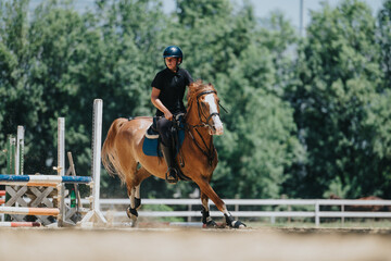 Obraz premium Equestrian rider practicing horse jumping outdoors on a sunny day at a riding arena, showcasing skill and agility in equestrian sports.