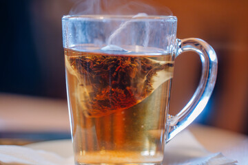 A close-up of a glass mug with a tea bag steeping in hot water, releasing steam in a cozy setting..