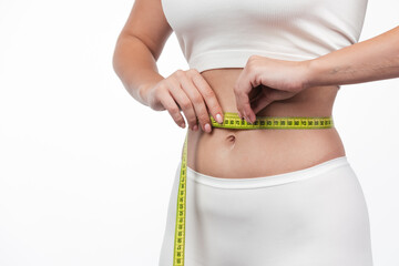 Cropped view of the sporty woman measuring waist with yellow tape against white background. Weight...