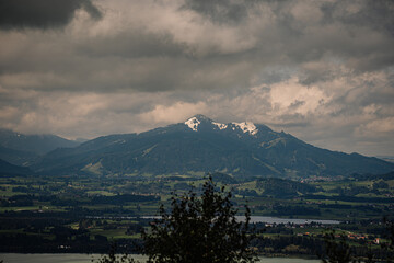 Mountainous landscape in Bavaria with snow-capped peaks, green valleys, and cloudy skies, creating a dramatic scenic view..