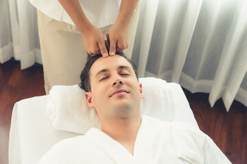 Obraz premium Caucasian man enjoying relaxing anti-stress head massage and pampering facial beauty skin recreation leisure in dayspa modern light ambient at luxury resort or hotel spa salon. Quiescent