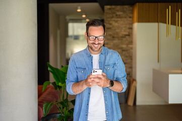 Positive male manager in glasses checking social media applications over mobile phone in modern office - Powered by Adobe