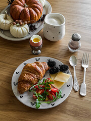 Delicious homemade breakfast - croissant, cheese, tomatoes, arugula, blackberries and cappuccino on a wooden table