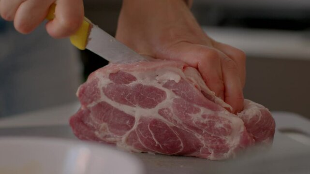 the cook's hands holding a knife cut a piece detailed closeup of a hand skillfully slicing fresh pork meat using a sharp knife within a kitchen setting