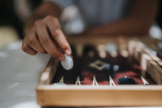 A hand strategically plays backgammon on a wooden board, highlighting focus and strategy in a traditional board game setting.