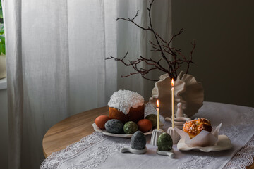 Easter concept. Traditional Easter pastries and colored eggs, candles on a wooden round table in the living room