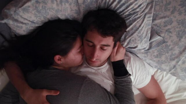 Couple resting together in bed, with the woman embracing the man. Eyes closed, suggesting a serene moment of closeness, comfort, and affection in a peaceful bedroom setting