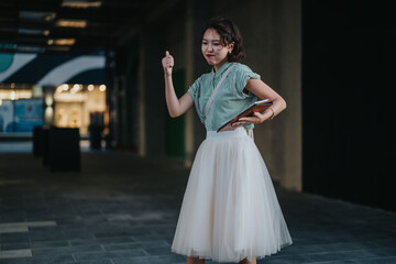 A young woman stands in an urban environment, confidently giving a thumbs up as she holds a tablet, symbolizing success and positivity.