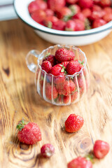 Strawberry harvest in a transparent cup on a wooden background, top view