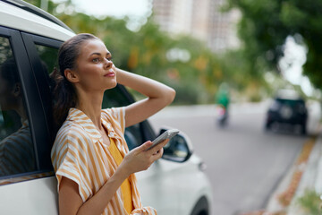 woman leaning against a car, looking at her phone, outdoors, urban background, bright colors, casual clothing, sunny day, relaxed atmosphere, city life, smartphone use © SHOTPRIME STUDIO