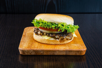 Grilled chicken Steak Burger with Lettuce, Tomato, and Cheese isolated on wooden board side view of fastfood on dark background