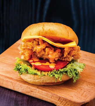 Spicy Chicken Zinger Burger with Lettuce, Tomato, Melted Cheese and Sauce isolated on wooden board closeup side view of fastfood on dark background