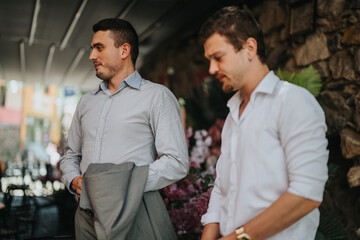 Two young men in relaxed attire have a conversation in an outdoor cafe setting. They appear to be...
