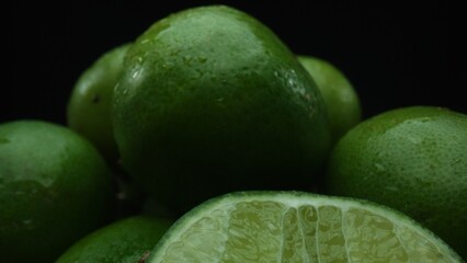 Slices of lime are meticulously arranged in a pile, set against a black background. Each lime slice is captured in stunning detail, its vibrant green hue and enticing texture. Close up. Comestible.