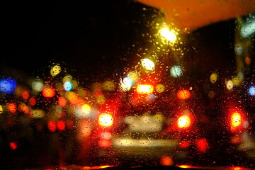 Blurry cars and lights in traffic. Rain drops on windshield glass window, raindrop texture in car, street color at night