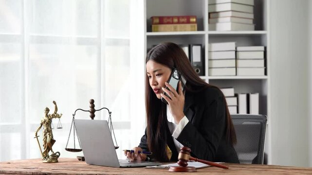Focused Attorney: A determined female lawyer in a professional suit, engrossed in a phone conversation while working on her laptop. The image exudes professionalism, expertise, and dedication.