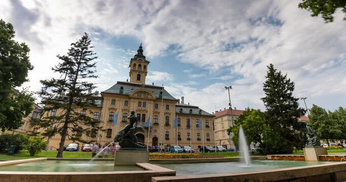 Szeged, Hungary - July 20, 2024: Szeged City Hall building, view from Szechenyi Square. Time-lapse, slide transition. Sunny day, medium cloudy sky.