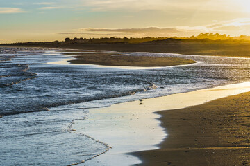 Golden sunset reflecting on the wet sand as waves gently roll onto the beach.