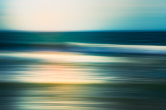 Blurry motion of ocean waves rolling toward the shore under a soft, cloudy sky.