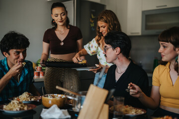 A group of friends gathers in the kitchen sharing a casual meal, enjoying food and conversation in a cozy home setting.