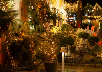Cute Christmas lights on European town street. Holiday atmosphere of illuminated sidewalk store entrance. Bright new year night. Shop porch decoration. Christmas tree glowing garland lights.